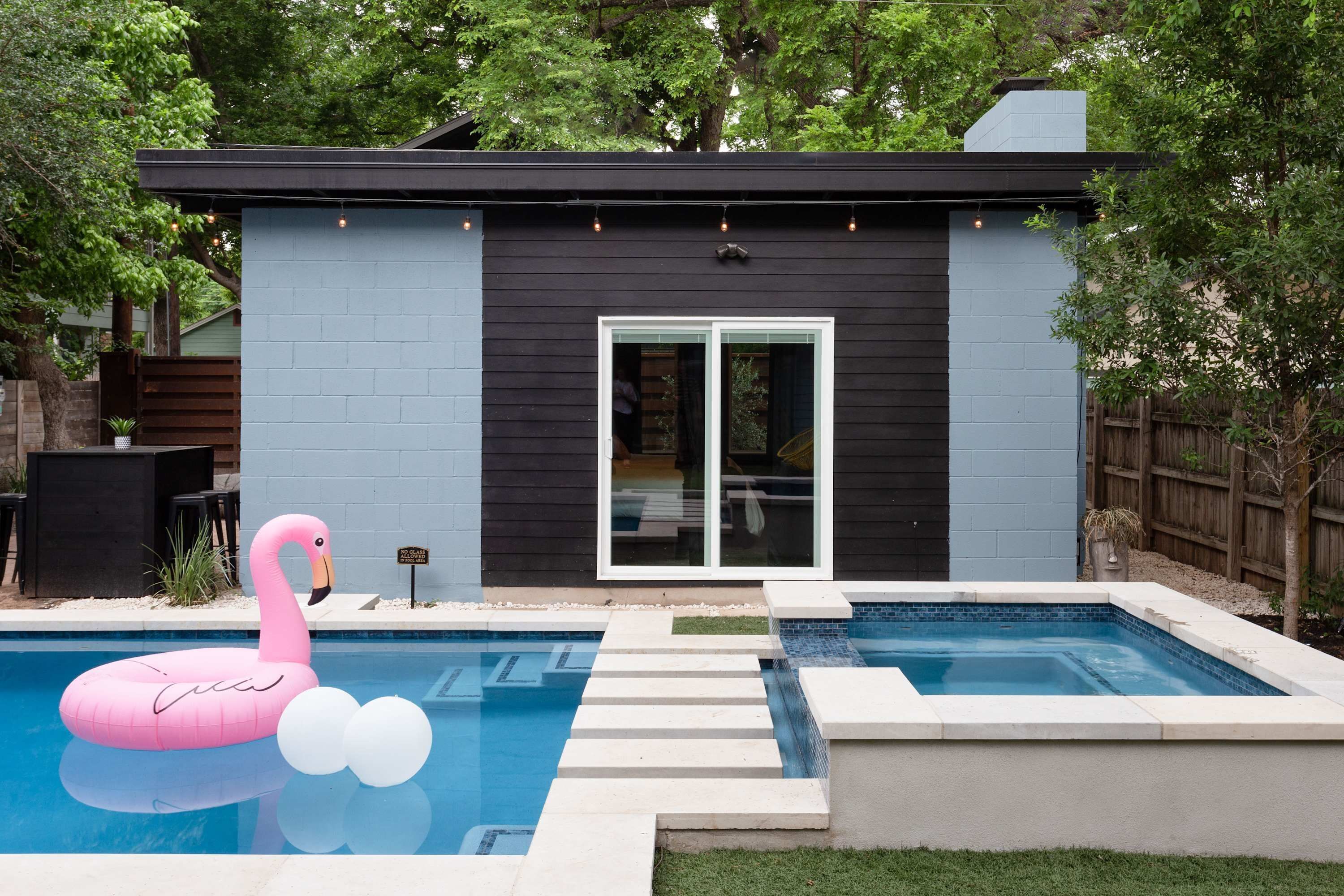 Una casa moderna con piscina, un flotador de flamenco rosa y una terraza de madera.
