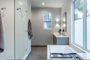 Une salle de bain moderne avec une douche à l’italienne, une grande fenêtre et un lavabo blanc.