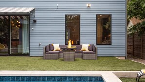 Ein modernes Haus mit grauer Fassade, einer Terrasse mit Feuerstelle und einem Schwimmbad.