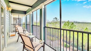 A balcony with a view of a green landscape, a table with chairs, and a railing.