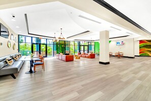 A spacious lobby with a modern design, featuring a seating area with sofas and chairs, a central coffee table, and a large window offering a view of greenery outside. - Upstay - Condo Near Disney w Games Pool Sauna (Winter Garden)