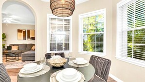 A dining area with a round table set for four, surrounded by wicker chairs. - Upstay - Modern Family Apartment w Pool Hot Tub (Winter Garden)