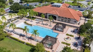 Vista aérea de un complejo turístico con piscina, palmeras y un pabellón.