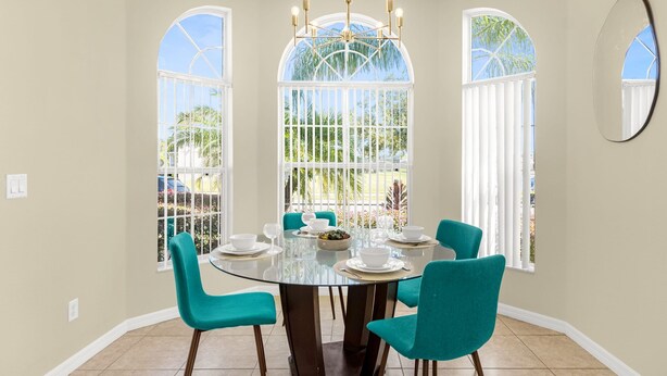 A dining area with a round glass table, teal chairs, and a chandelier. - Upstay - New Home Near Disney w Private Pool BBQ (Kissimmee)