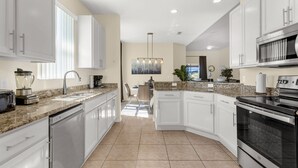 A modern kitchen with white cabinets, granite countertops, a built-in dishwasher, a stainless steel oven, and a large island with seating. - Upstay - New Home Near Disney w Private Pool BBQ (Kissimmee)