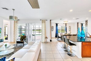 A spacious living area with a sofa, a coffee table, and a dining area with bar stools. - Waterfront Pet-friendly Home w Pool-spa-games-bbq (Kissimmee)