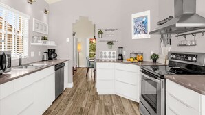 Eine moderne Küche mit weißen Schränken, einem Edelstahlherd und einem eingebauten Backofen. Es gibt eine Frühstückstheke mit einer Kaffeemaschine und einem Spülbecken.