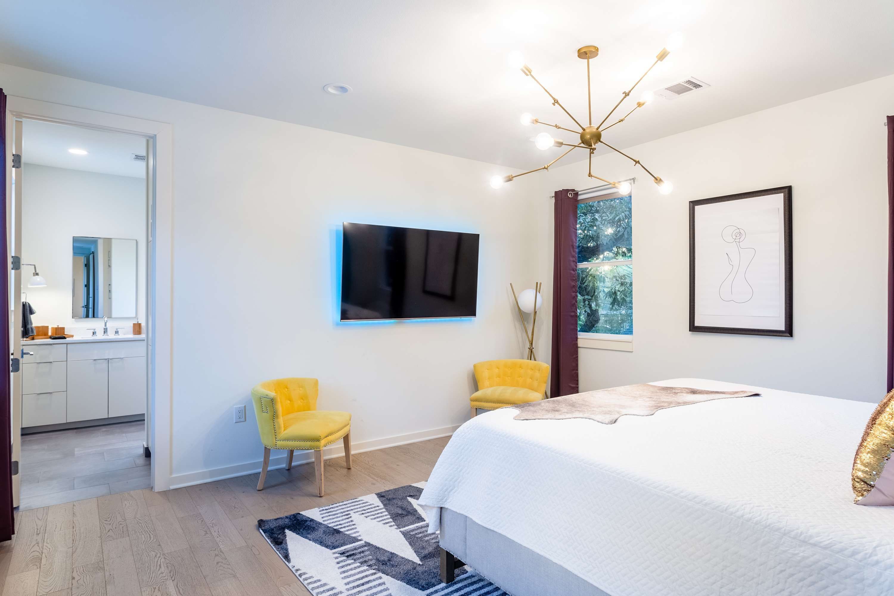 A modern bedroom with a large bed, a mounted TV, and two yellow chairs.