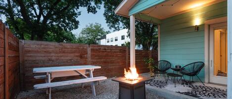 An outdoor patio with a wood-burning stove, picnic table, and chairs.