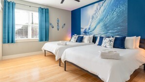 A hotel room with two beds, a ceiling fan, a large ocean wave mural, and a window with curtains. - Upstay - East Austin Home w Yard Games Fire Pit (Austin)