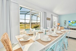 Un coin repas avec une table dressée pour quatre personnes, de grandes fenêtres et une vue sur un paysage verdoyant.