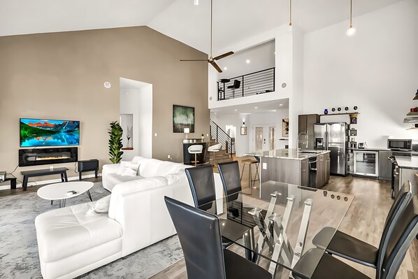 A modern open-plan living and dining area with a white sofa, glass dining table, and black chairs.