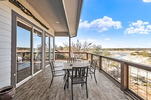 A wooden deck with a table and chairs, large sliding glass doors, and a view of the landscape.