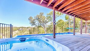 A hot tub on a wooden deck with a view of trees and houses in the background. - Upstay - Lakeside Getaway - Pool Hot Tub Games (Lakeway)