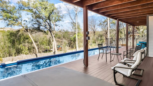 A covered outdoor area with a pool, lounge chairs, and a view of trees and hills. - Upstay - Lakeside Getaway - Pool Hot Tub Games (Lakeway)