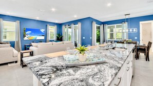 Une cuisine moderne dotée d’un grand îlot central, de murs bleus et d’un coin repas avec une table et des chaises.