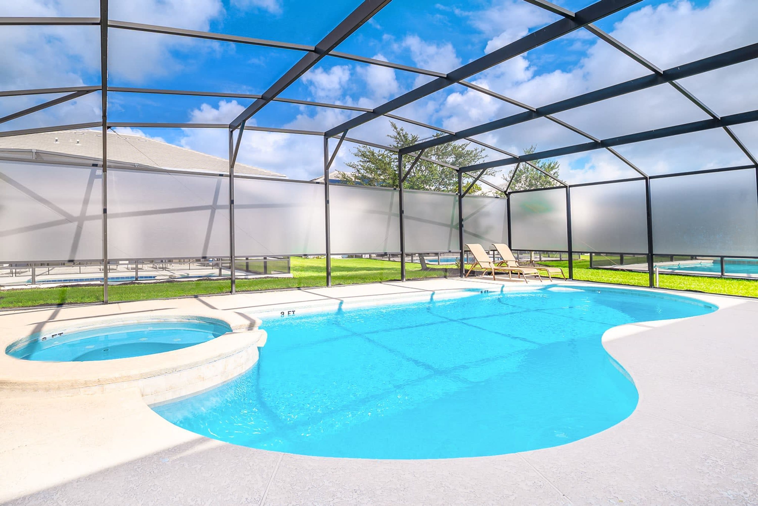 A pool with a clear blue water feature, surrounded by a covered area with a metal frame and a view of a grassy lawn and trees in the background.