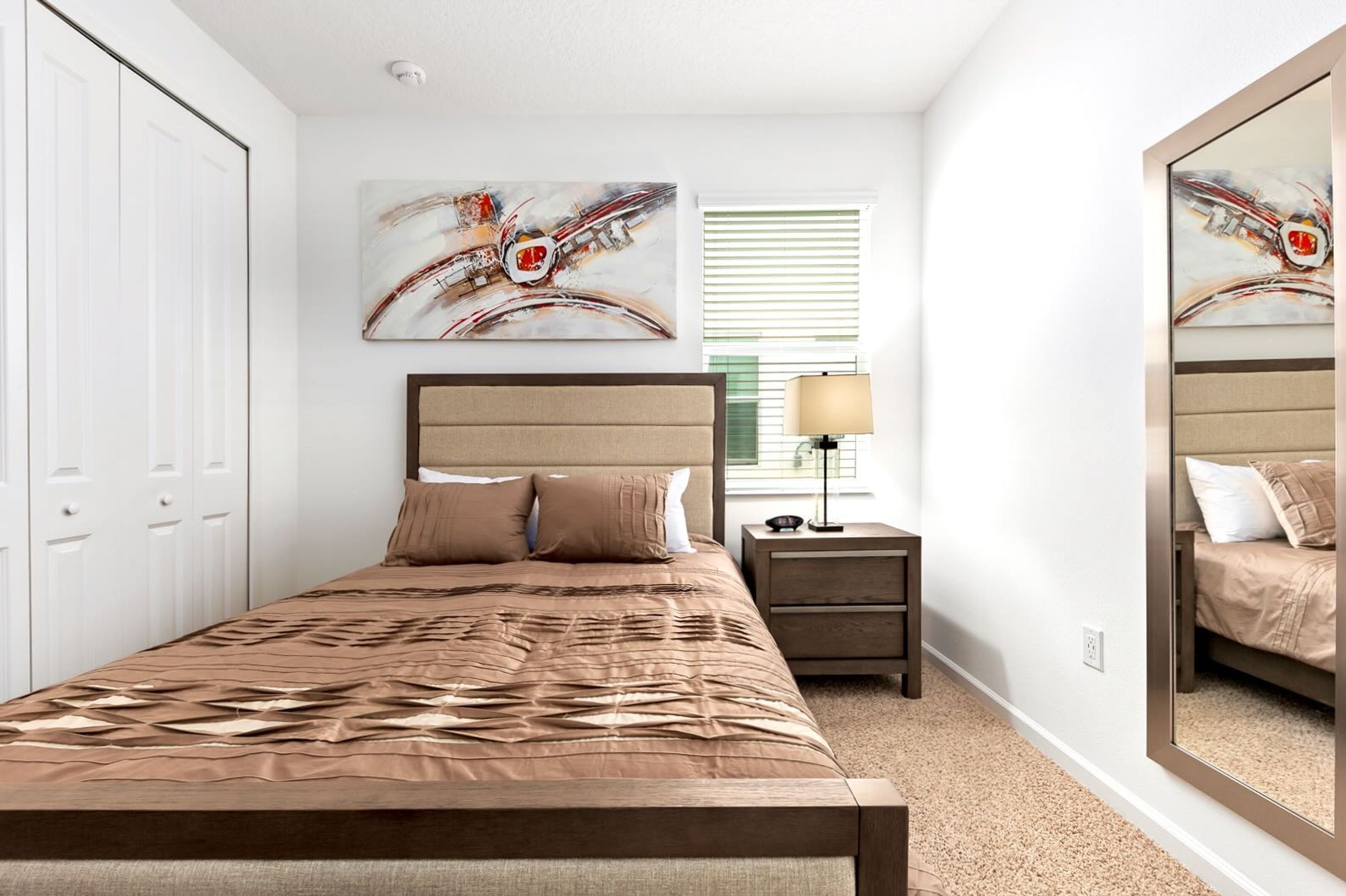 Quarto com cama, mesa de cabeceira, abajur, espelho e obras de arte na parede.