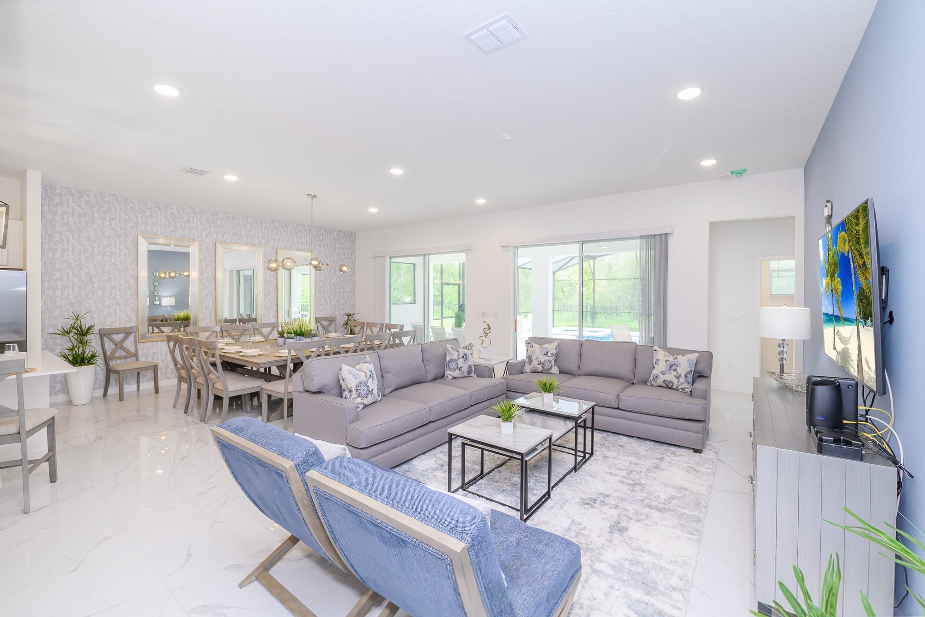 A spacious living room with a grey sofa, a blue armchair, and a dining area with a table and chairs.