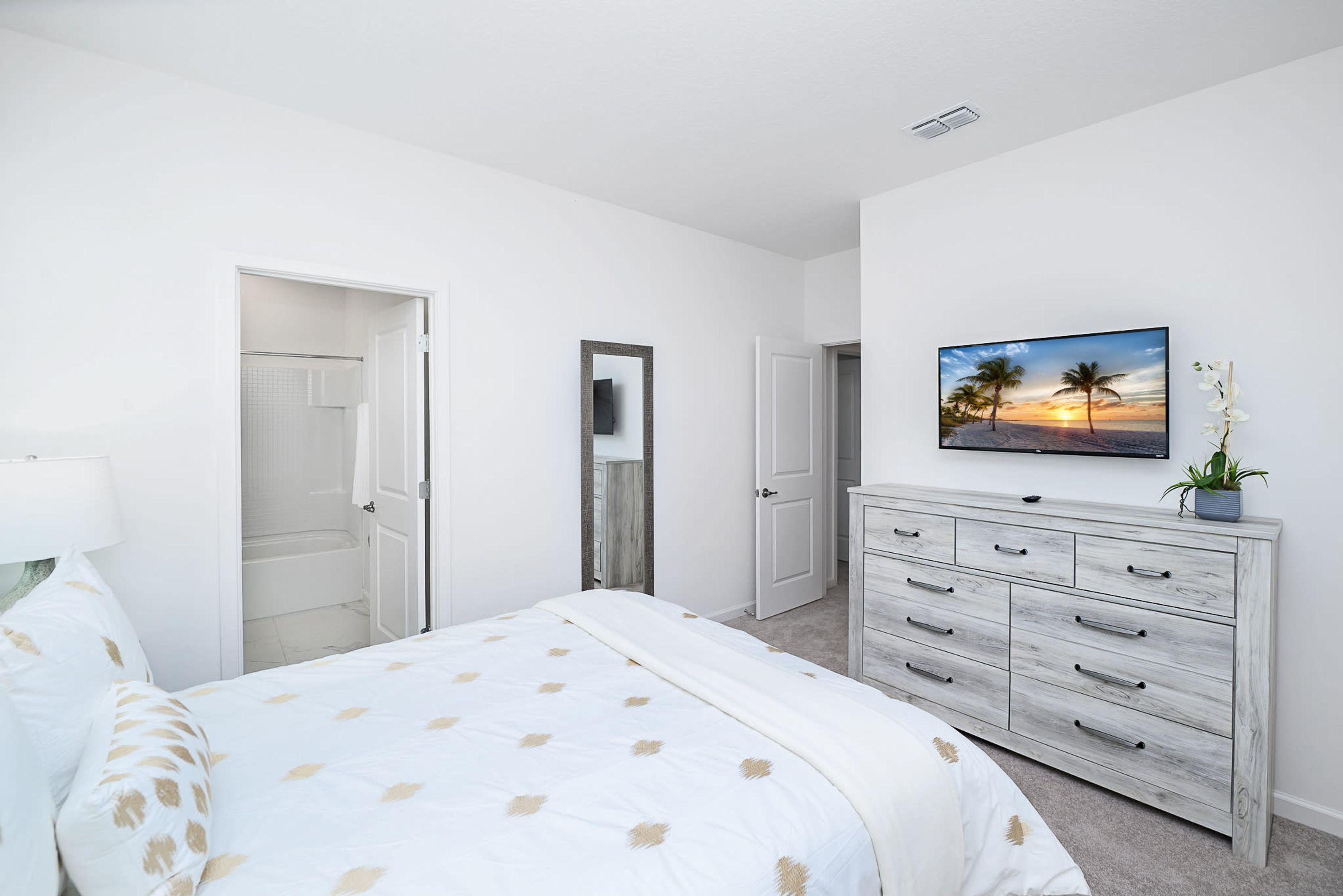 A bedroom with a bed, a dresser, a mirror, and a wall-mounted TV.