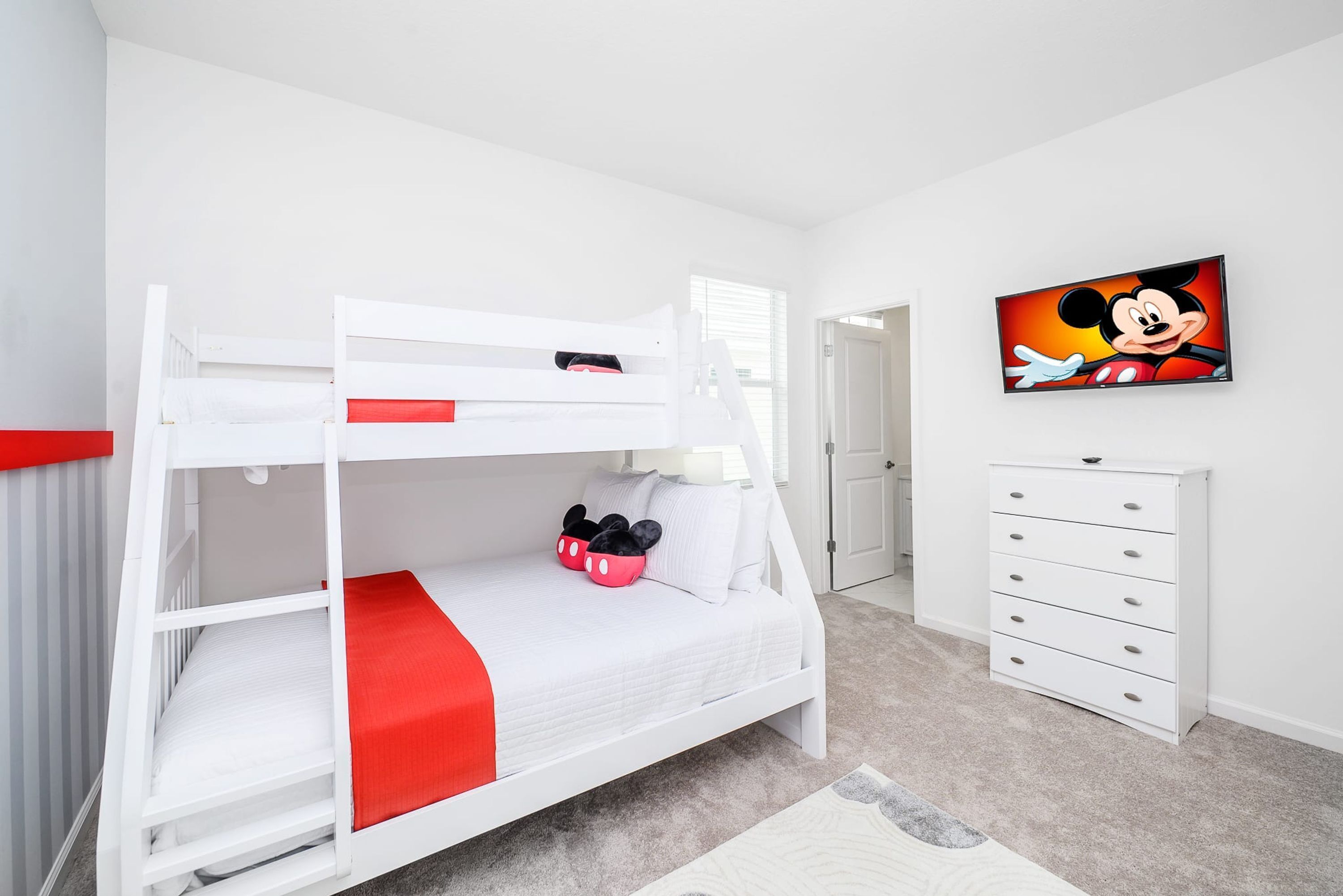 A bunk bed with a red runner, a Mickey Mouse painting, and a white dresser in a bedroom.