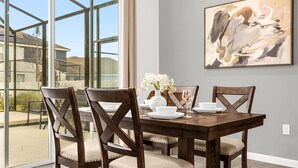 A dining area with a large window, a table set for four, and a painting on the wall. - Upstay - Ultimate Orlando Oasis w Pool and Hot Tub (Kissimmee)