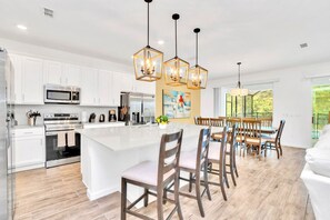 A modern kitchen with white cabinets, stainless steel appliances, a large island, and wooden chairs. - Upstay - 19-guest Resort Home w Pool Hottub Disney (Kissimmee)