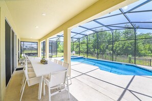 Eine überdachte Terrasse mit Pool, weißem Tisch und Stühlen und Blick auf Grünflächen.