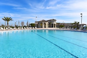 A large, clear swimming pool with lounge chairs and a building in the background.