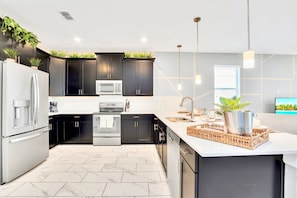 A modern kitchen with dark cabinets, stainless steel appliances, and a white countertop. - Pool Hot Tub Resort Waterslides - Sleeps 16 (Davenport)