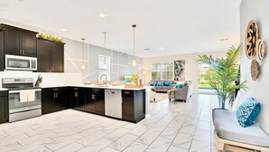 Una cocina moderna con armarios oscuros, una isla central y un área de comedor con sofá y mesa.