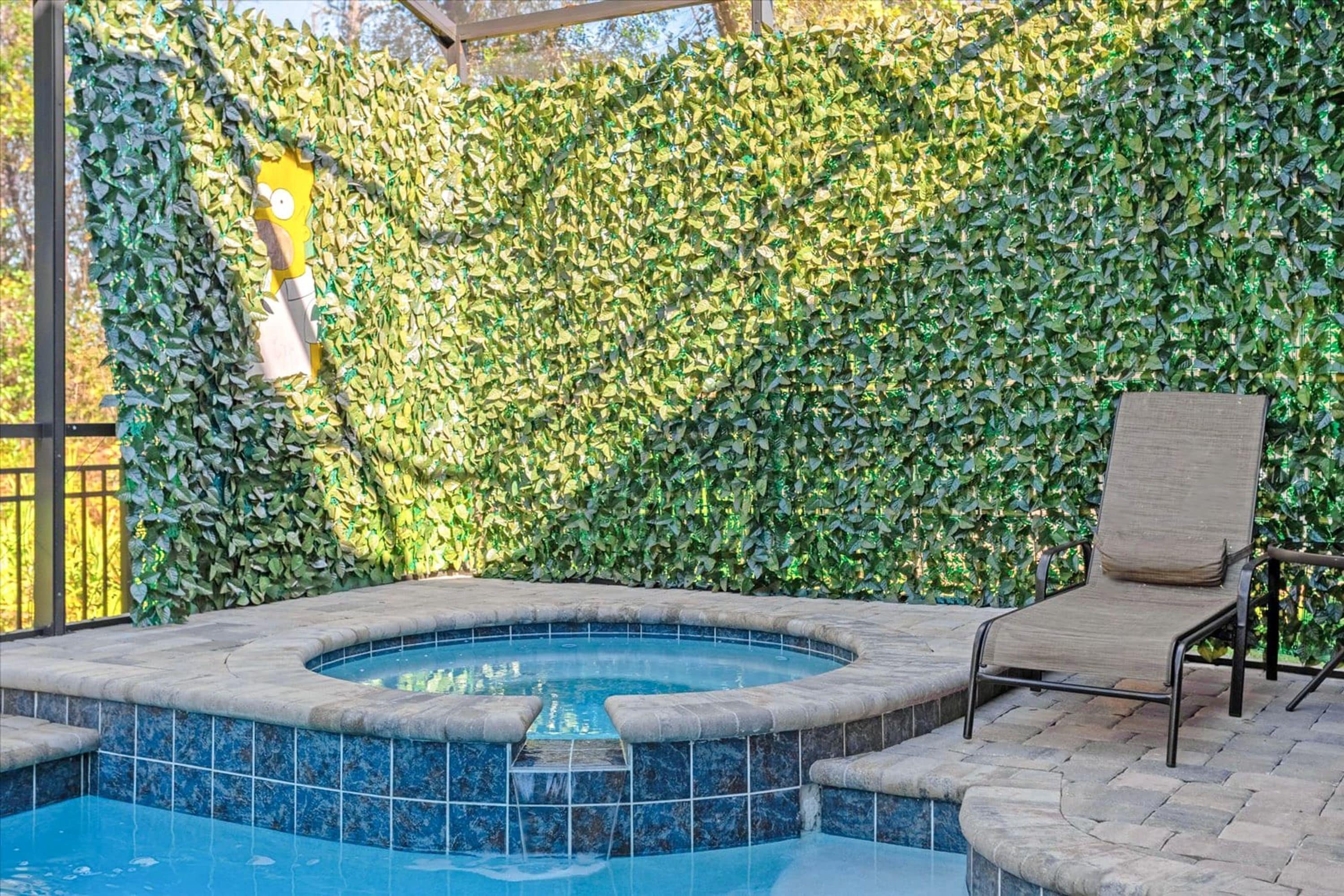 Una bañera de hidromasaje con borde de azulejos, rodeada de un patio de piedra y una silla.