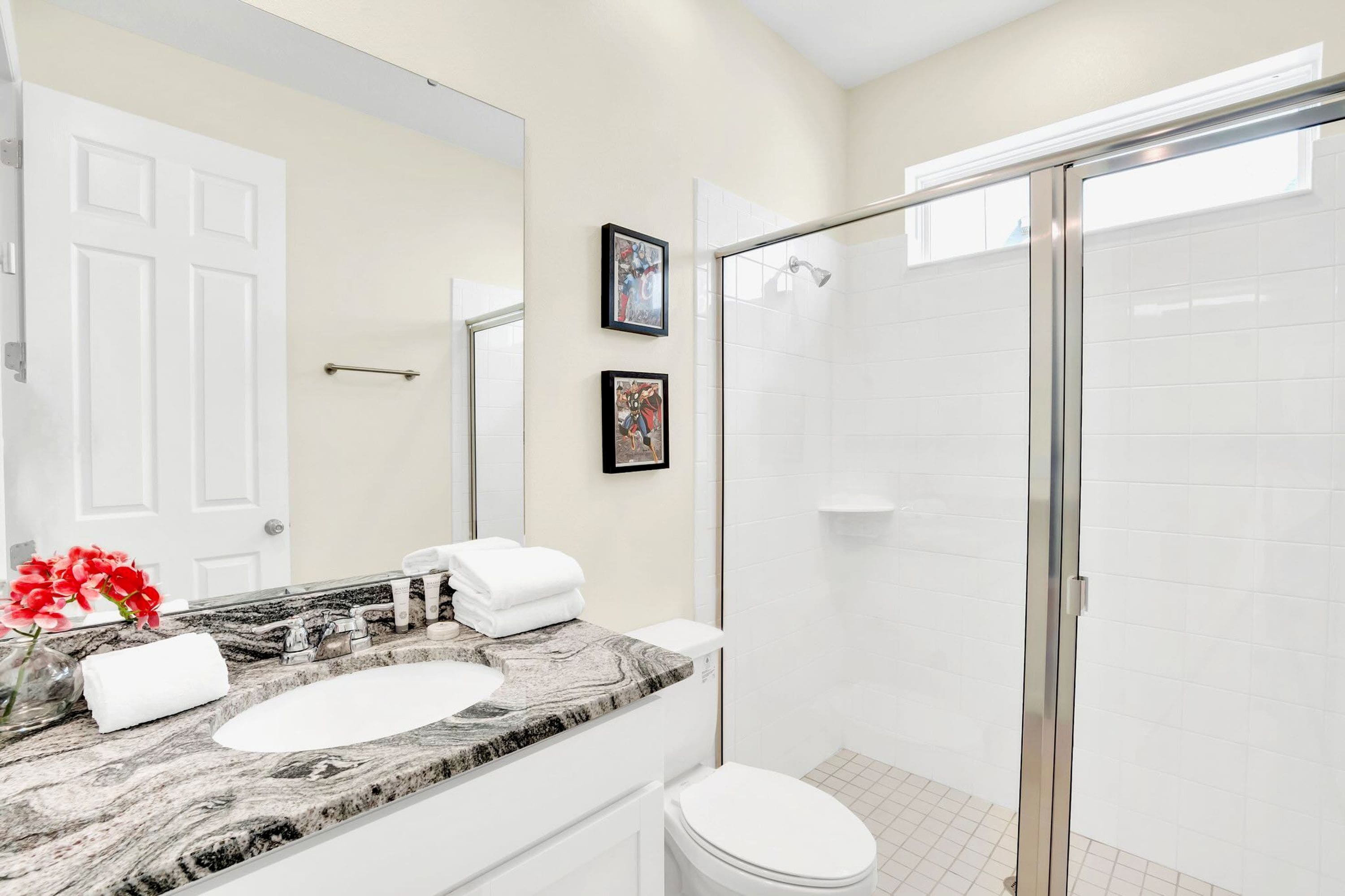 A bathroom with a marble sink, a toilet, a shower with a glass door, and two framed pictures on the wall.