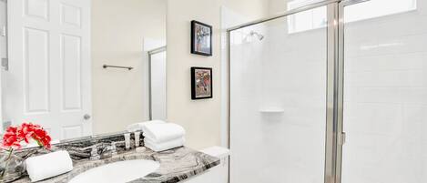 A bathroom with a marble sink, a toilet, a shower with a glass door, and two framed pictures on the wall.