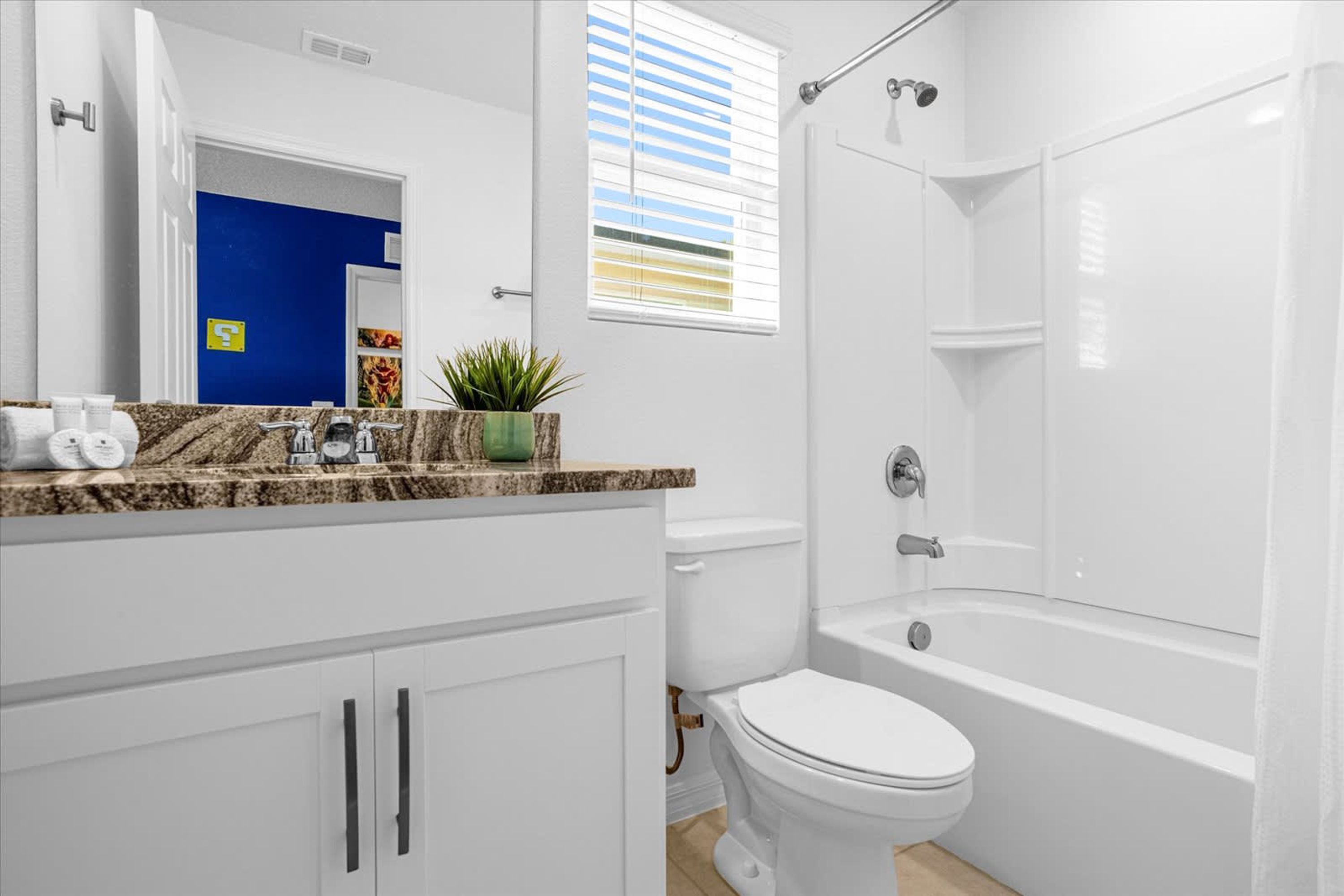 A modern bathroom with a white toilet, a bathtub, and a shower. There is a sink with a marble countertop and a potted plant on it.