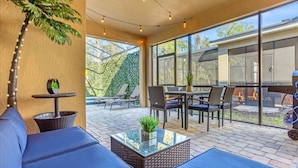 A covered patio area with outdoor furniture, a glass-top coffee table, and string lights. - Upstay - 20-guest Home w Hot Tub-pool-bbq-arcade (Kissimmee)