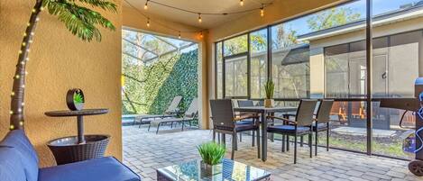 A covered patio area with outdoor furniture, a glass-top coffee table, and string lights.