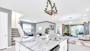 A modern kitchen with a marble island, built-in dishwasher, and a hanging plant chandelier. - Upstay - 20-guest Home w Hot Tub-pool-bbq-arcade (Kissimmee)