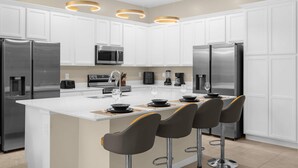 A modern kitchen with white cabinets, stainless steel appliances, and a central island with bar stools. - Upstay - 30ppl Home w Theme Rooms-games-pool-spa (Kissimmee)