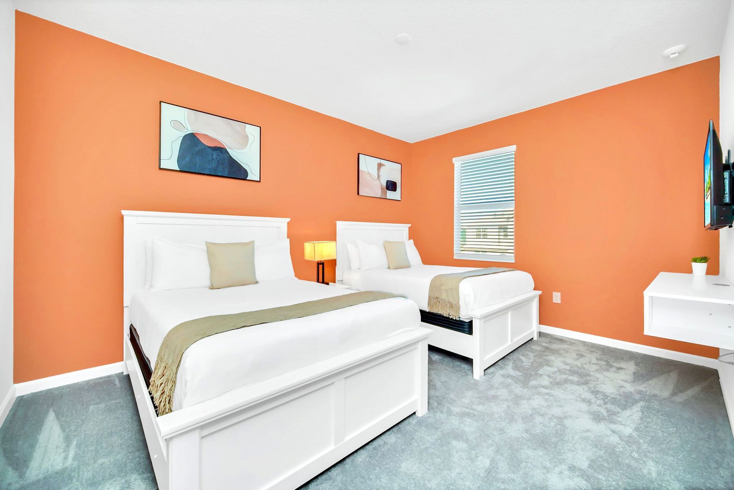 A hotel room with two beds, a TV, a desk, and artwork on the walls.