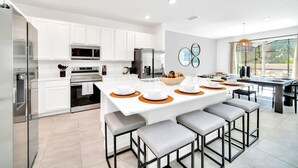 A modern kitchen with white cabinets, stainless steel appliances, and a central island with stools. - Upstay - Modern Pool Home w Games - Sleeps 18 (Kissimmee)