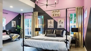A modern bedroom with a large bed, a desk, and a chair. There are curtains, a plant, and artwork on the walls. - Pool Hottub Magic School Bus 5 Mins to Downtown (Austin)