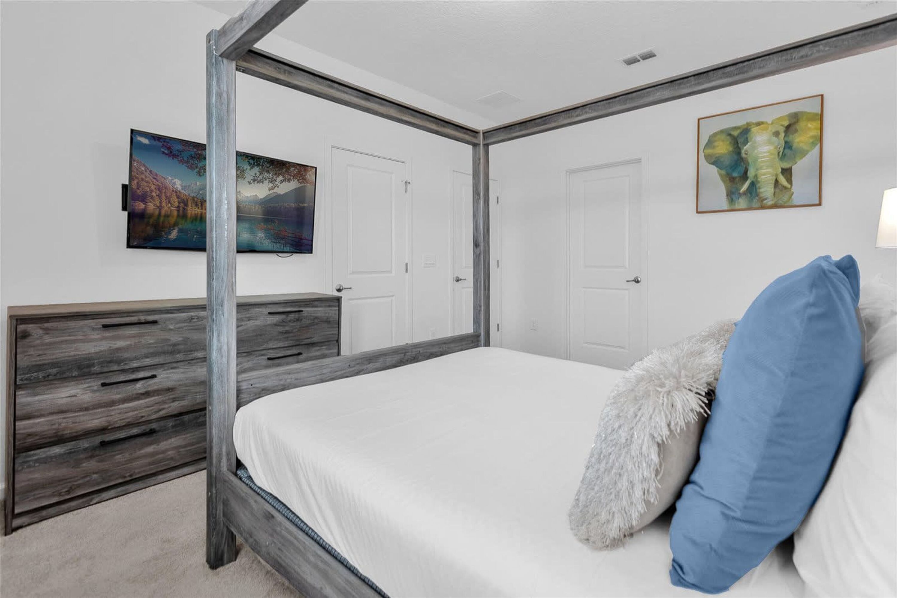 A bedroom with a four-poster bed, a wooden dresser, and two doors.