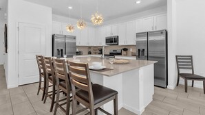 A modern kitchen with white cabinets, stainless steel appliances, and a central island with seating. - Upstay - Gator Getaway w Pool Hot Tub Theme Rooms (Kissimmee)