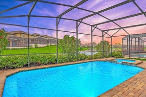 A swimming pool with a glass enclosure, surrounded by greenery and a view of residential buildings. - Spacious 8BR Home for Large Group - Pool Games (Kissimmee)