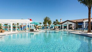 Piscina com espreguiçadeiras e guarda-sóis, cercada por palmeiras e um edifício com telhado em azulejos.