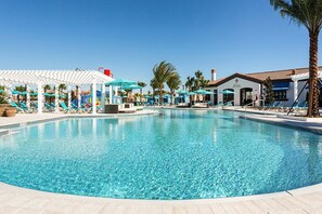 A swimming pool with lounge chairs and umbrellas, surrounded by palm trees and a building with a tiled roof. - Windsor at Westside Resort Home w Pool Hot Tub (Kissimmee)