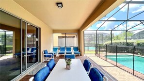 Eine sonnige Terrasse mit Pool, blauen Sitzgelegenheiten und einem weißen Tisch.