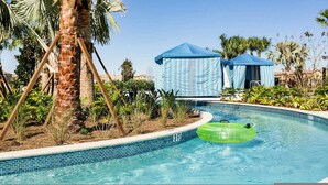 Una piscina con un círculo inflable verde, palmeras y tiendas de campaña azules al fondo.