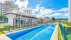 A modern hotel with a large swimming pool, glass-enclosed rooms, and a view of surrounding buildings. - Upstay - NEW Build - Viva Jaco Condo w Epic Views (Jacó)